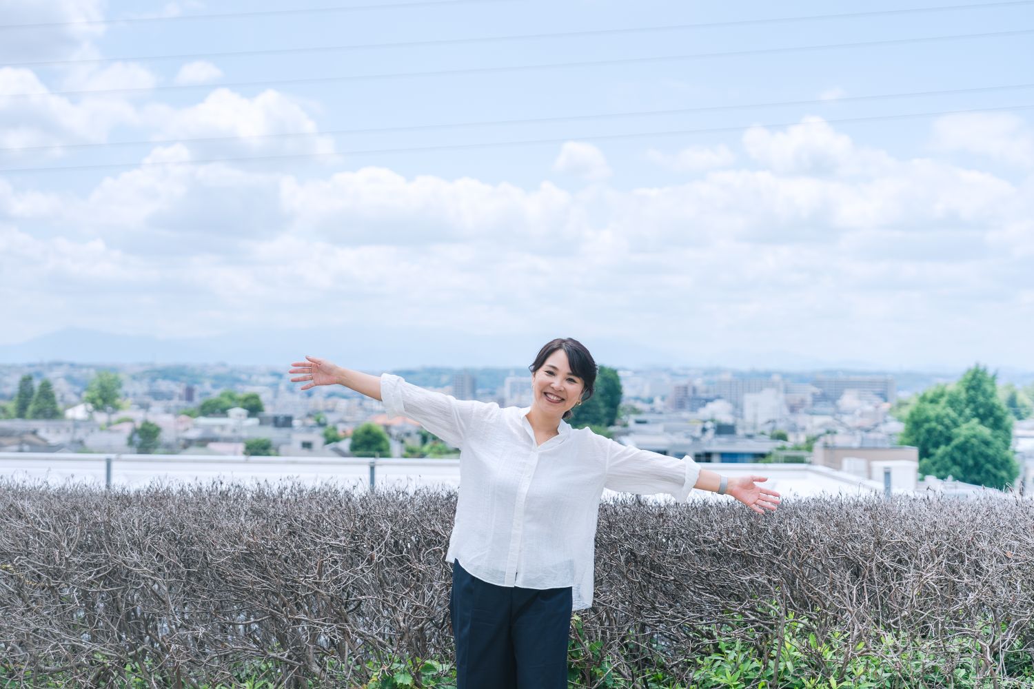 世田谷の青空と街並みを背景に立つ株式会社千織不動産 代表・加納千織